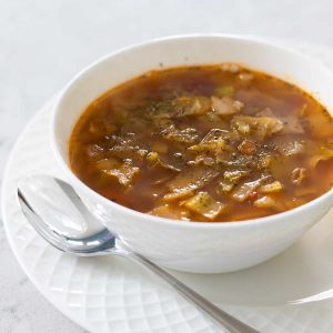 A white bowl of cabbage soup with a spoon on the side.