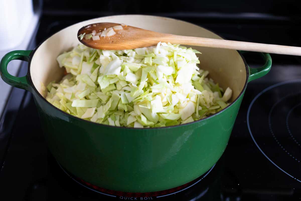 The raw cabbage looks like it won't fit in the pot, a wooden spoon shows height for reference.