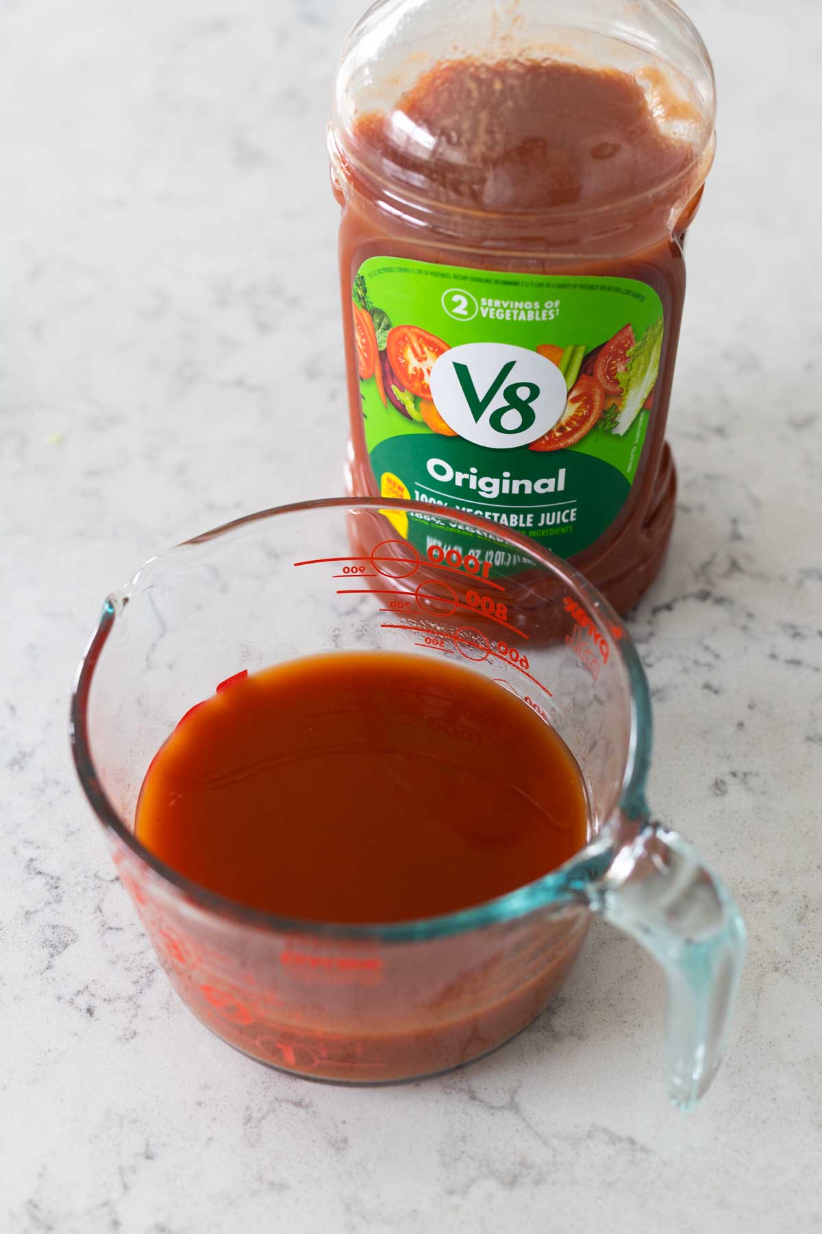 A bottle of V8 juice next to a measuring cup.