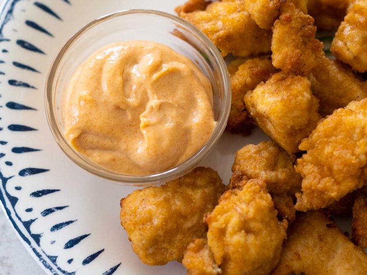 The yum yum sauce is in a dipping cup on a plate with chicken nuggets.
