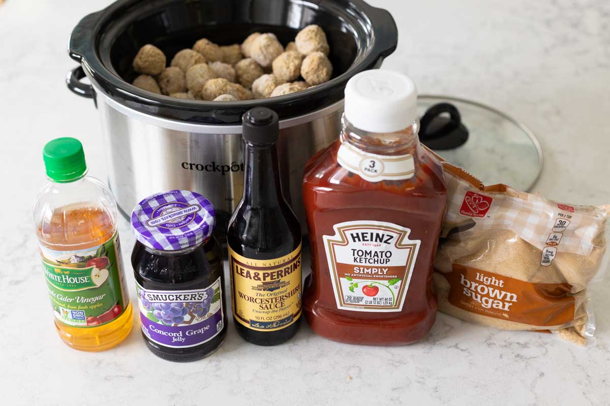 The ingredients are on the counter in front of the slowcooker filled with frozen meatballs.