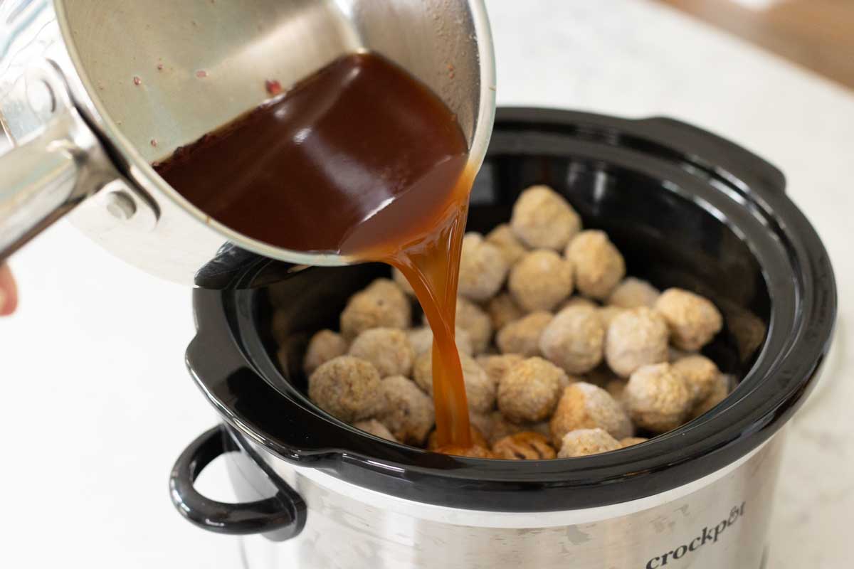 The cooked sweet and sour sauce is being poured over the frozen meatballs inside the slowcooker.