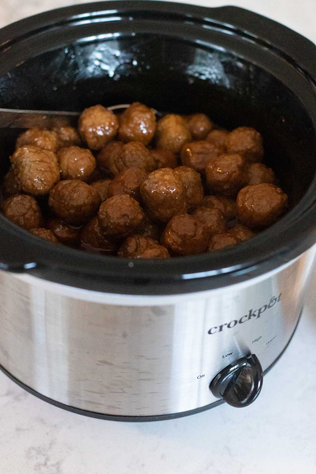 The sweet and sour sauce has been stirred over the meatballs in the Crockpot.