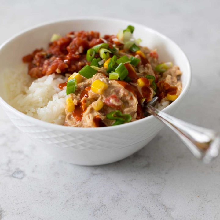 A bowl of rice is topped with crockpot creamy chicken made with cream cheese and topped with salsa and green onions.