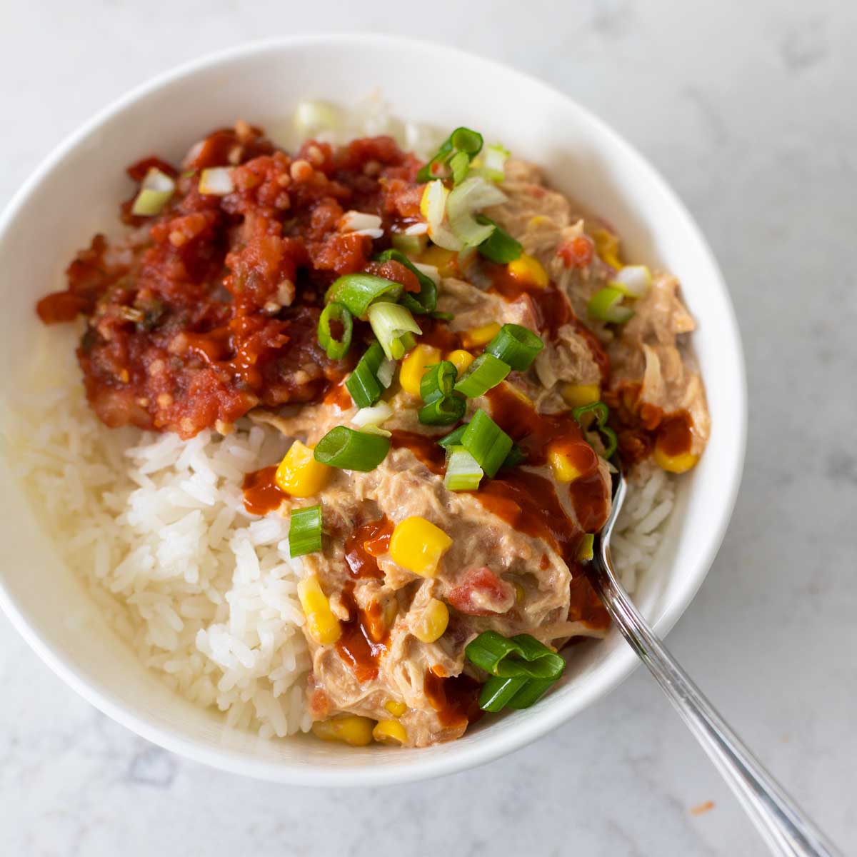 A bowl of rice is topped with the crockpot creamy chicken, salsa, and green onions.