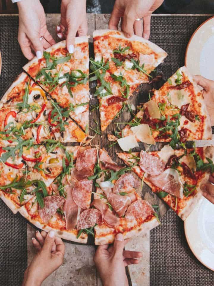 Hands reaching in to take slices of pizza on a family table.
