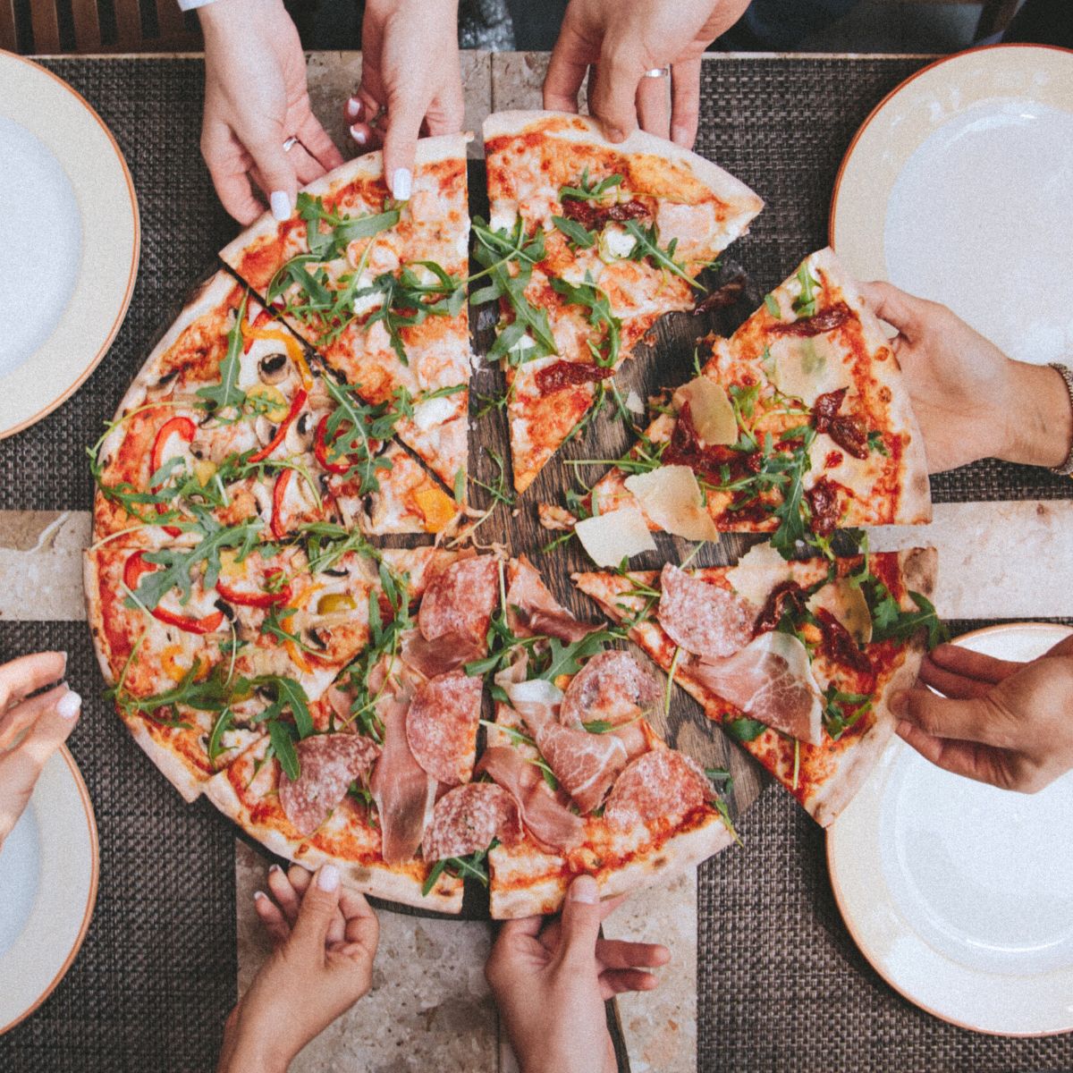 Hands reaching in to take slices of pizza on a family table.