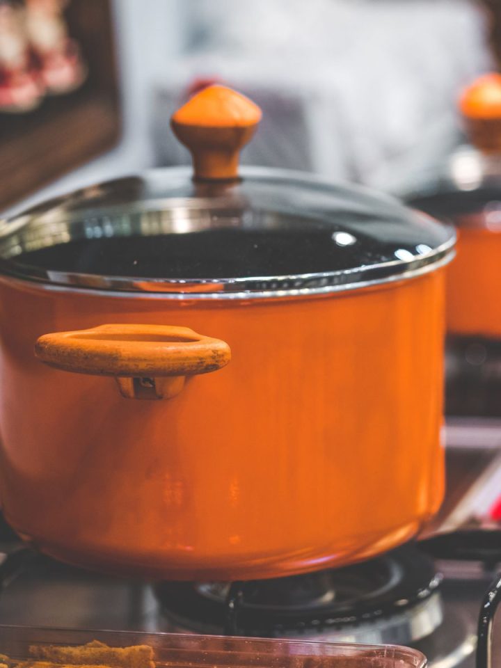 An orange pot on the stovetop is cooking a family dinner.