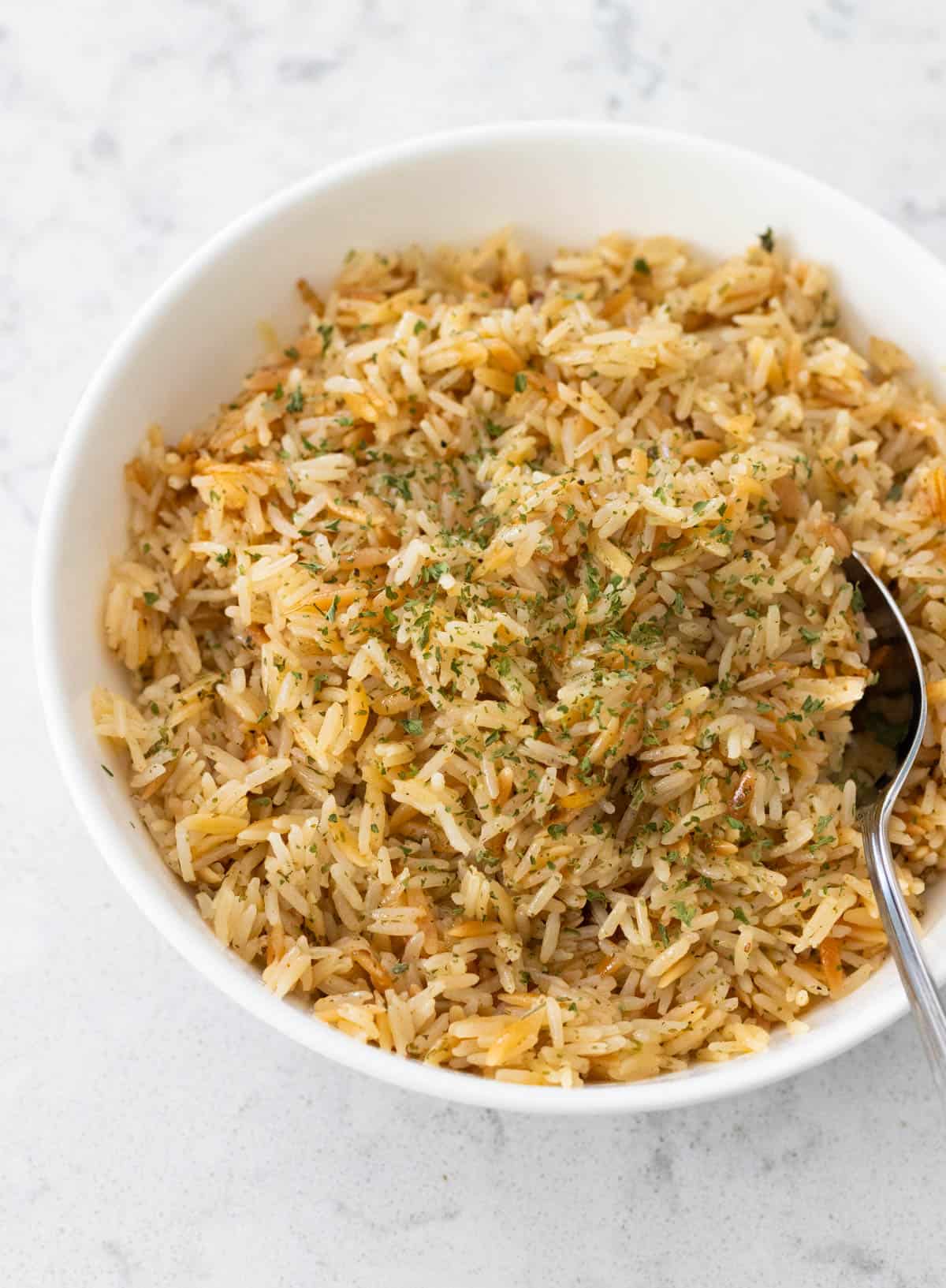 The finished rice pilaf is being served in a white bowl at the table.