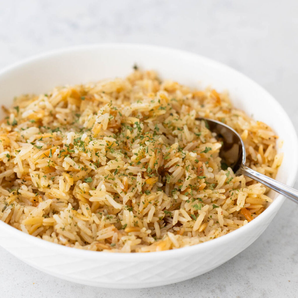 The buttery rice pilaf is in a white bowl with a spoon.