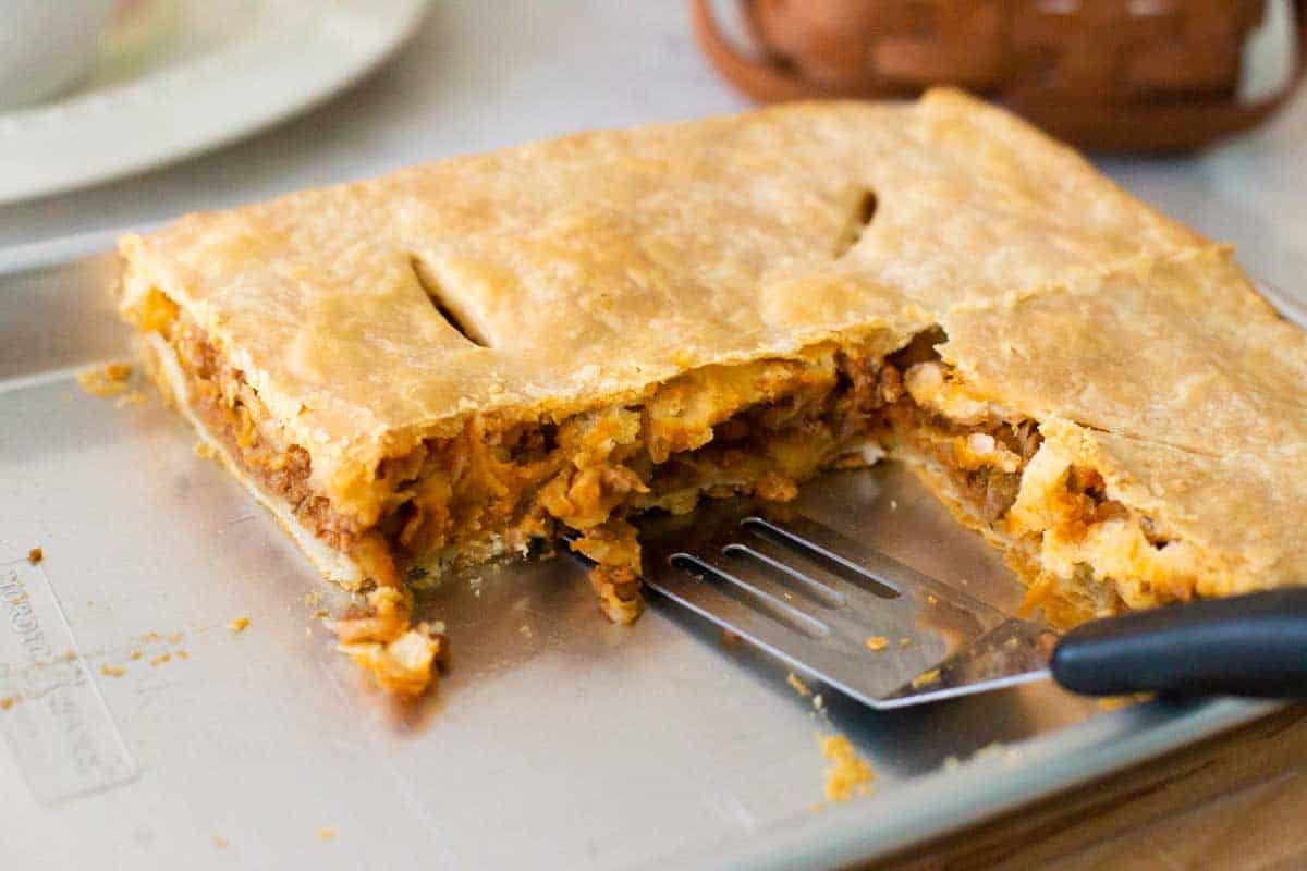 The pie has been cut into squares, a spatula is ready to serve a piece.