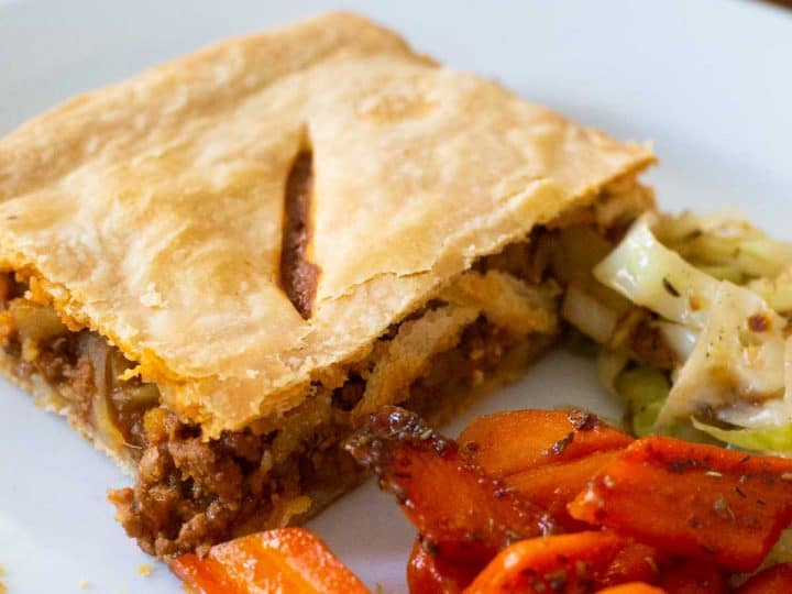 A square of Irish meat pie on a plate with carrots and cabbage.