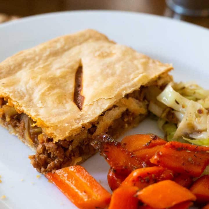 A square of Irish meat pie on a plate with carrots and cabbage.