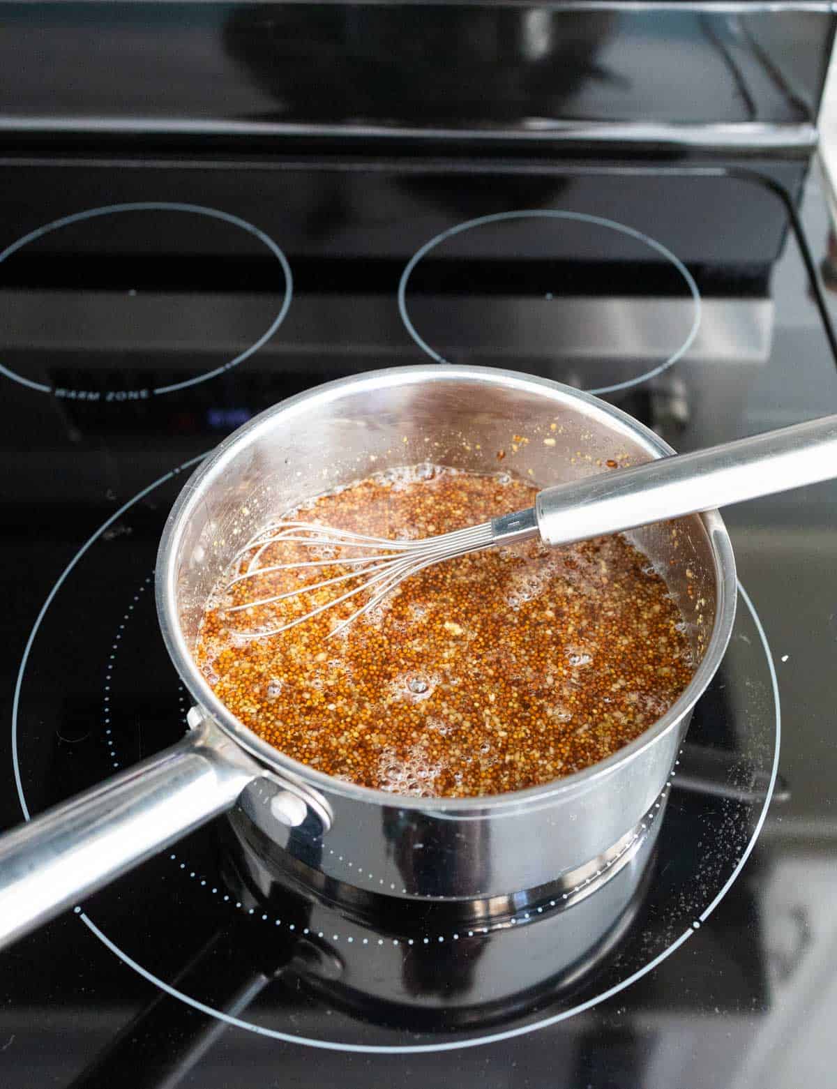 The saucepan has a whisk stirring the glaze on the stovetop.