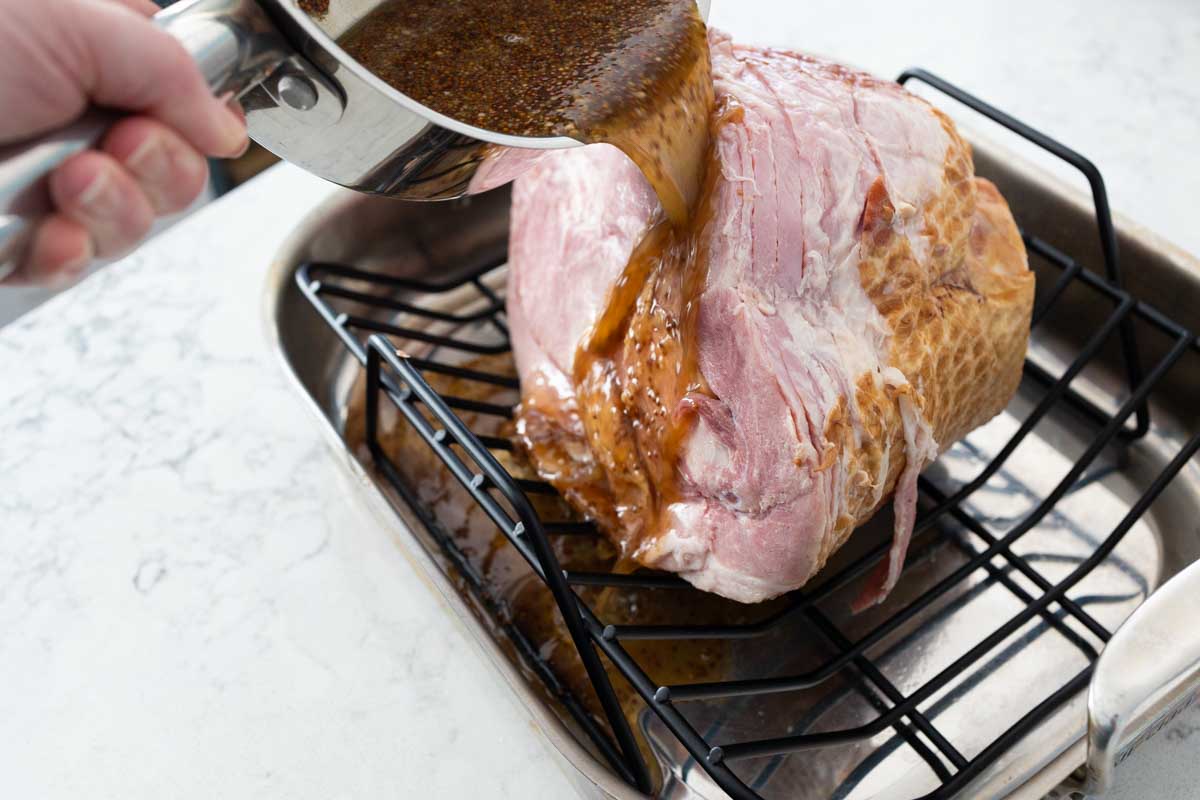 The saucepan is being held over the ham and the glaze is pouring down over it.