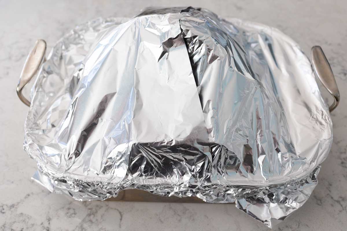 The roasting pan has been completely sealed with aluminum foil over the ham.