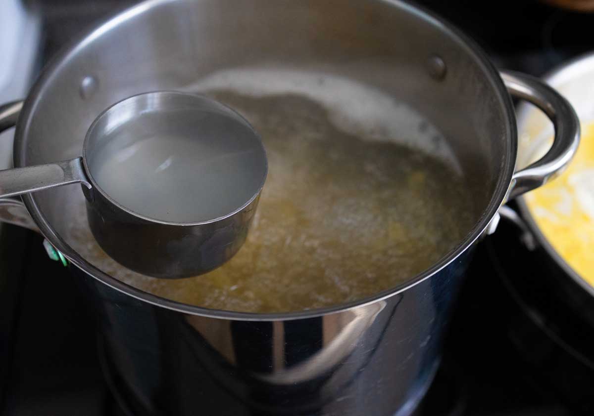 A measuring cup has strained some of the pasta cooking water from the pot.