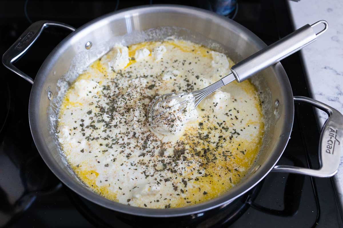 The sauce has been seasoned with herbs and is being whisked.