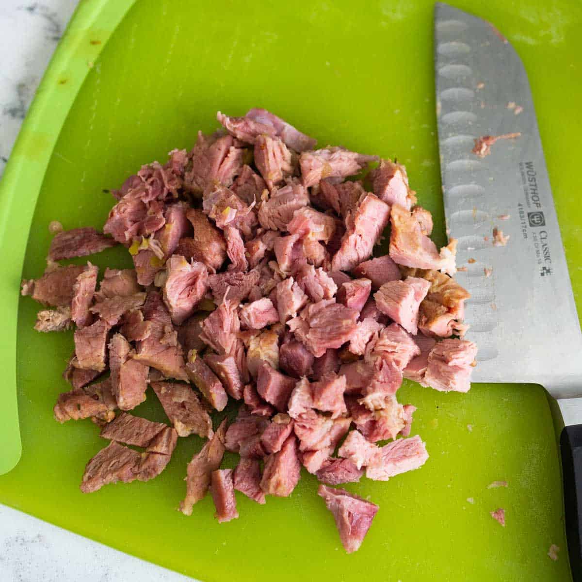 The ham from the ham bone has been pulled off with a fork and diced with the knife that is next to it on the cutting board.