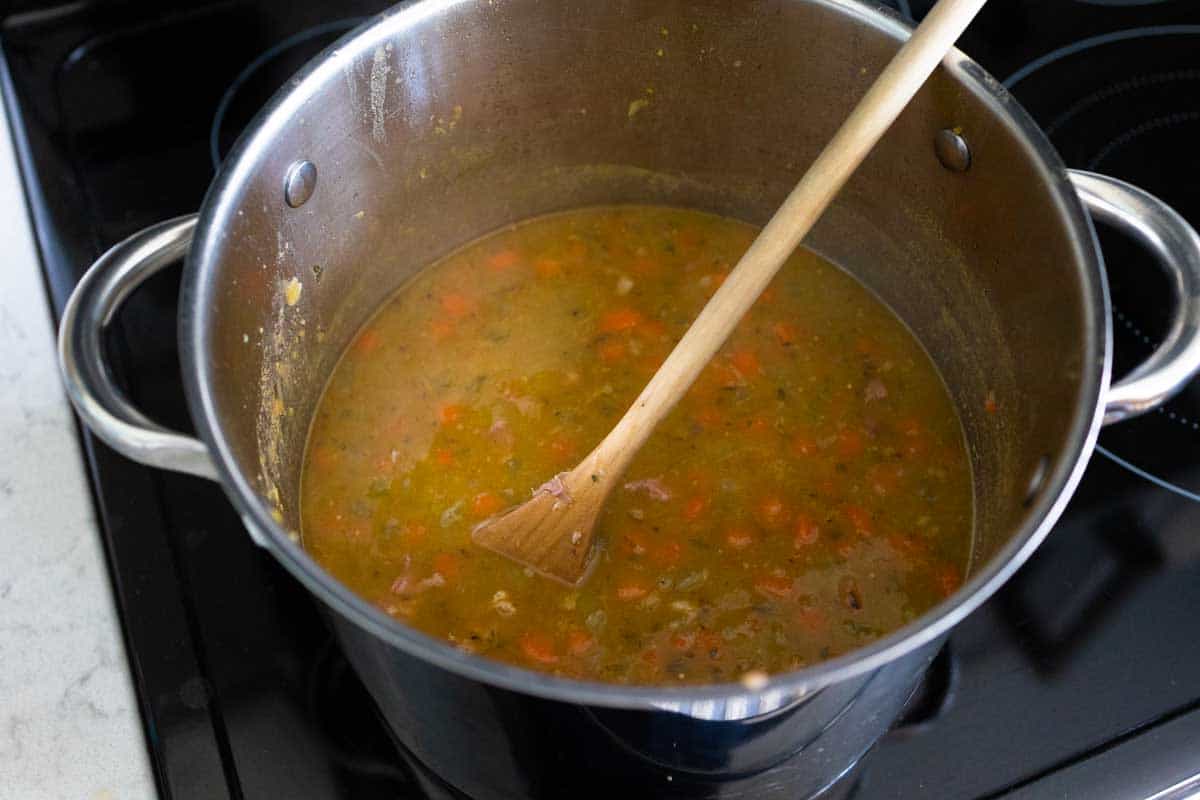 The peas have been cooked until the starch has thickened the broth. A spoon is stirring to show texture.