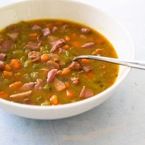 A bowl of chunky split pea and carrot soup has chunks of ham floating in the broth.