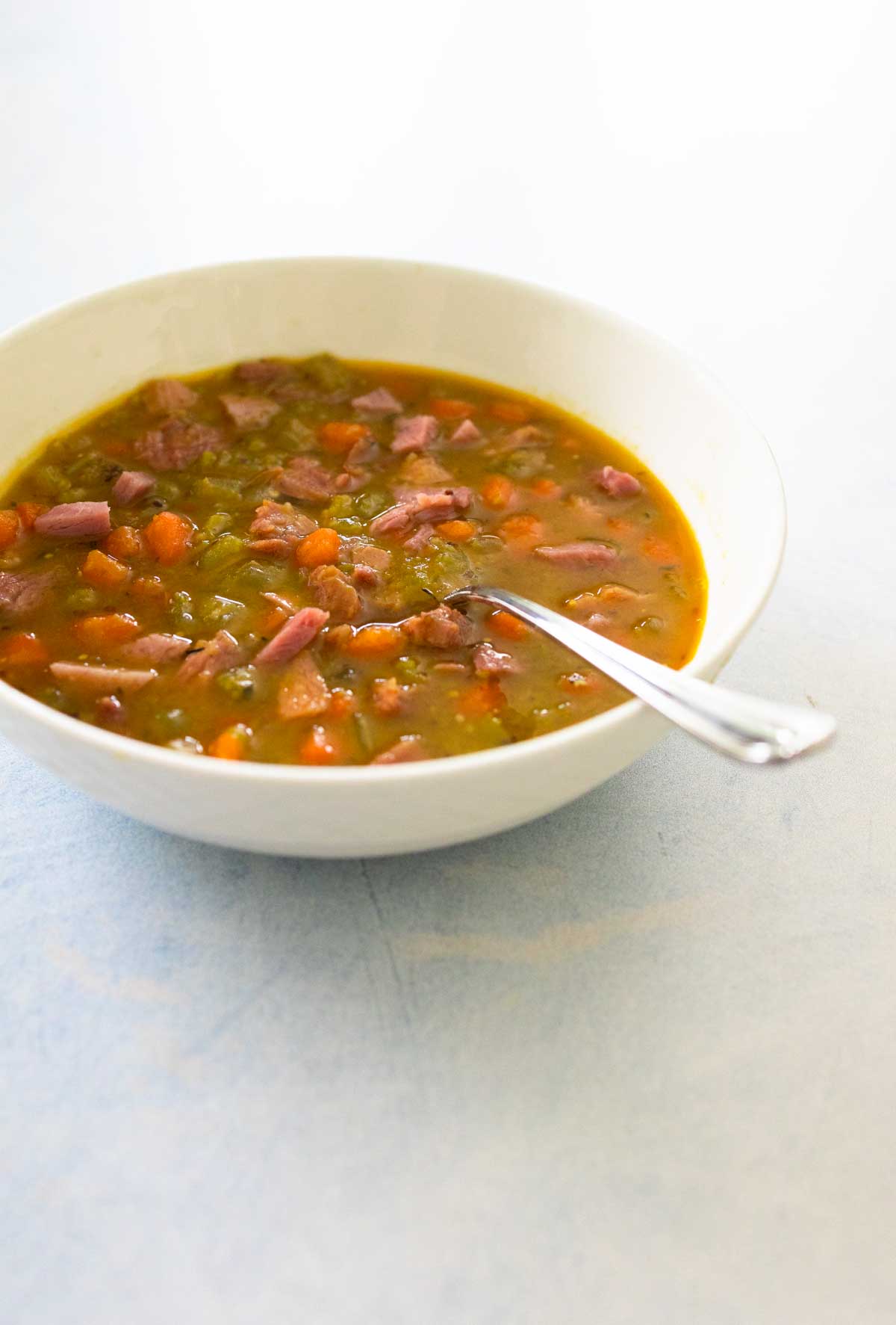 A bowl of chunky split pea and carrot soup has chunks of ham floating in the broth.