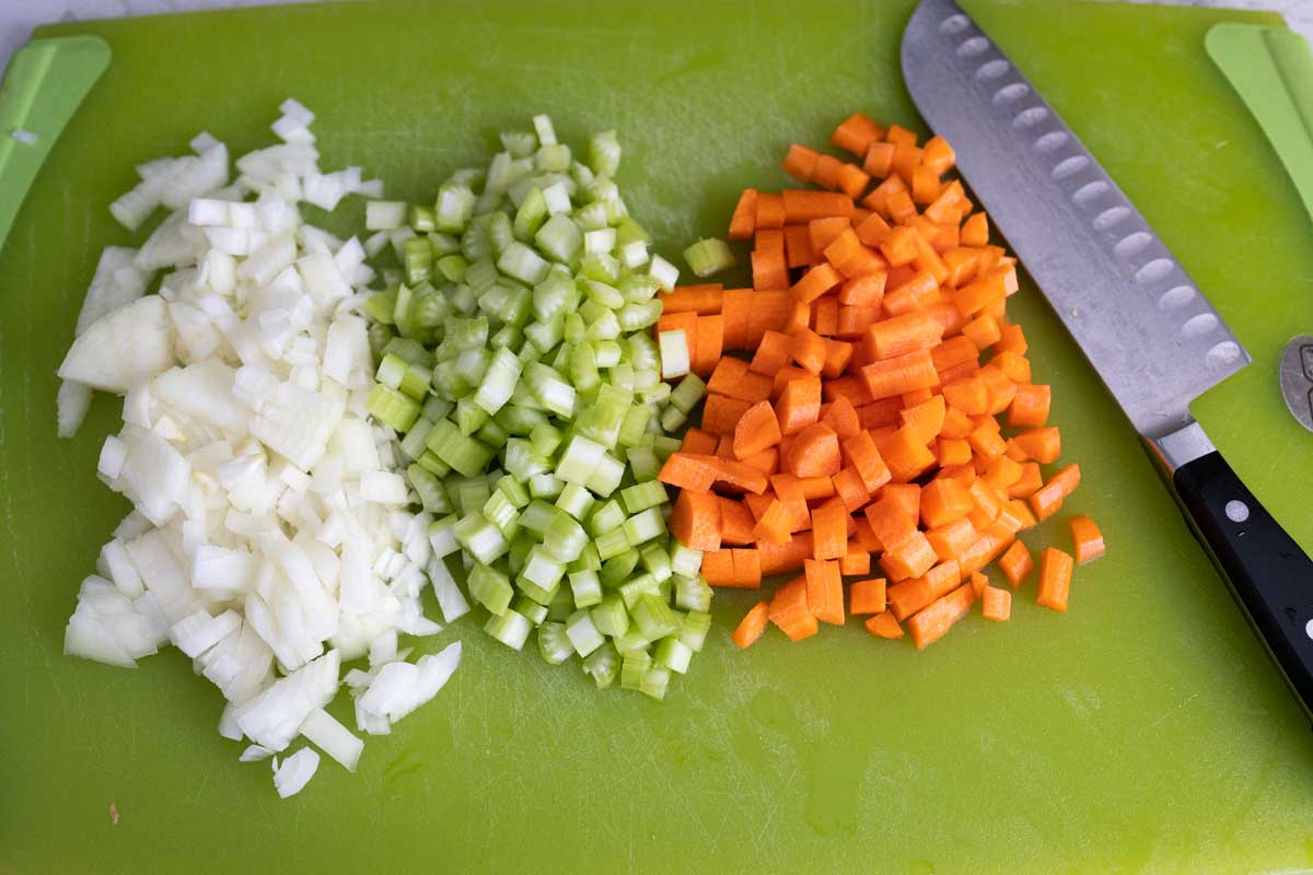 The base of the soup starts with these chopped vegetables on a cutting board next to a chef knife.