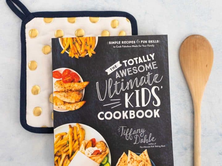 A copy of a kids' cookbook sits on a polka dot pot holder next to a wooden spoon.