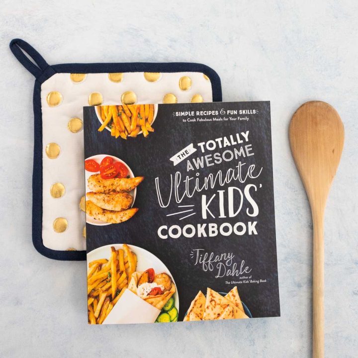 A copy of a kids' cookbook sits on a polka dot pot holder next to a wooden spoon.