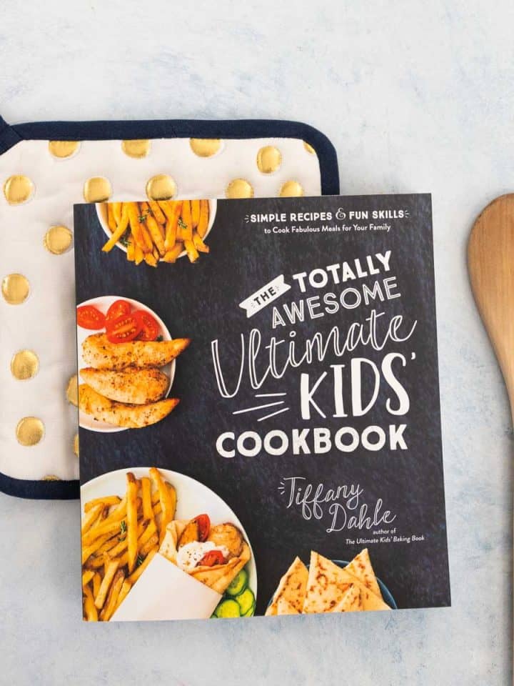 A copy of a kids' cookbook sits on a polka dot pot holder next to a wooden spoon.