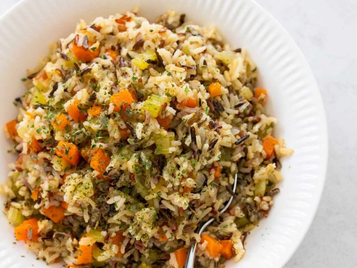 A white bowl is filled with wild rice pilaf, chunks of carrots and celery are peeking out.