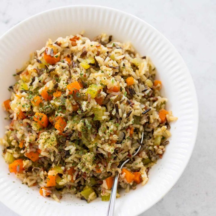 A white bowl is filled with wild rice pilaf, chunks of carrots and celery are peeking out.