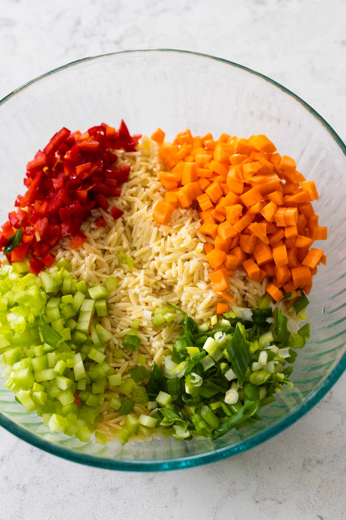The mixing bowl has the cooked orzo pasta topped with chopped carrots, celery, red pepper, and green onions.