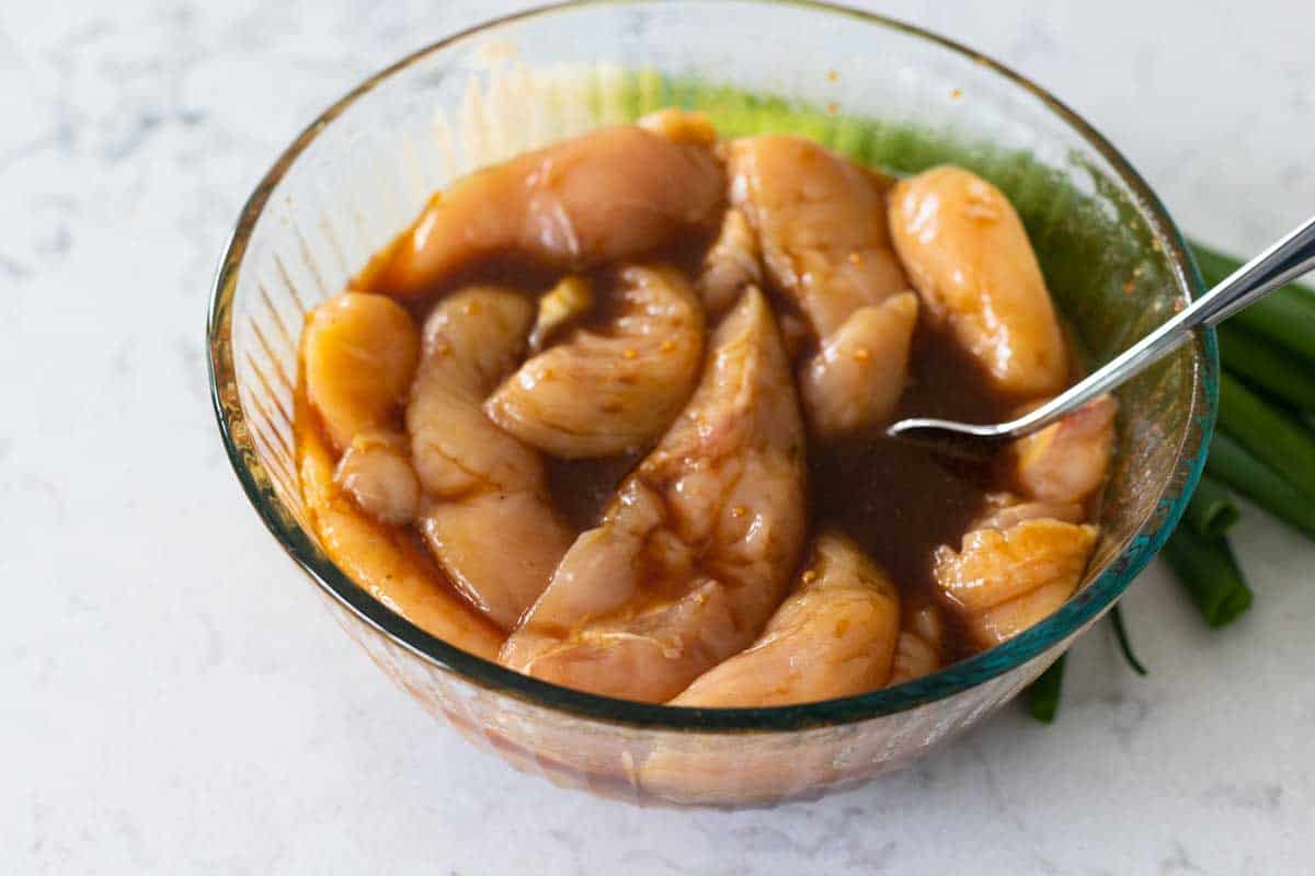 A mixing bowl has half the marinade soaking 2 pounds of chicken tenderloins.