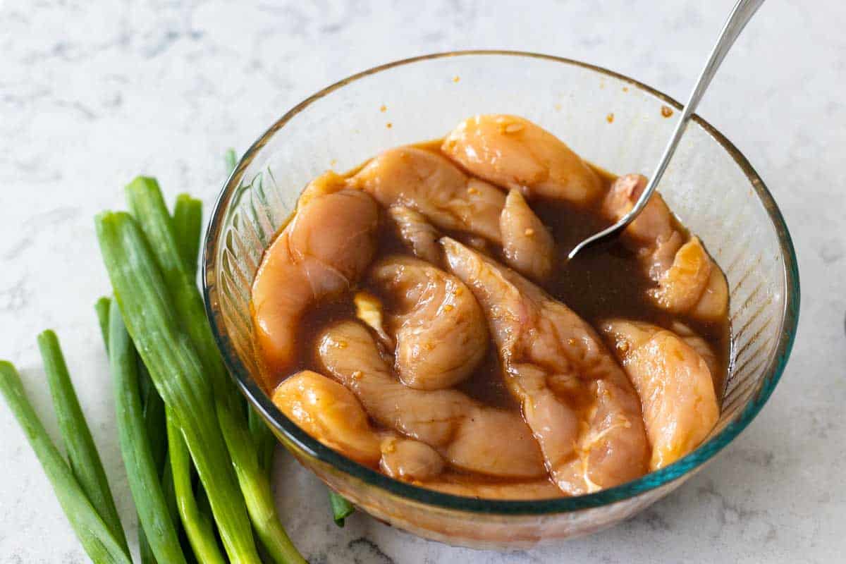 A mixing bowl shows chicken tenderloins in a marinade.