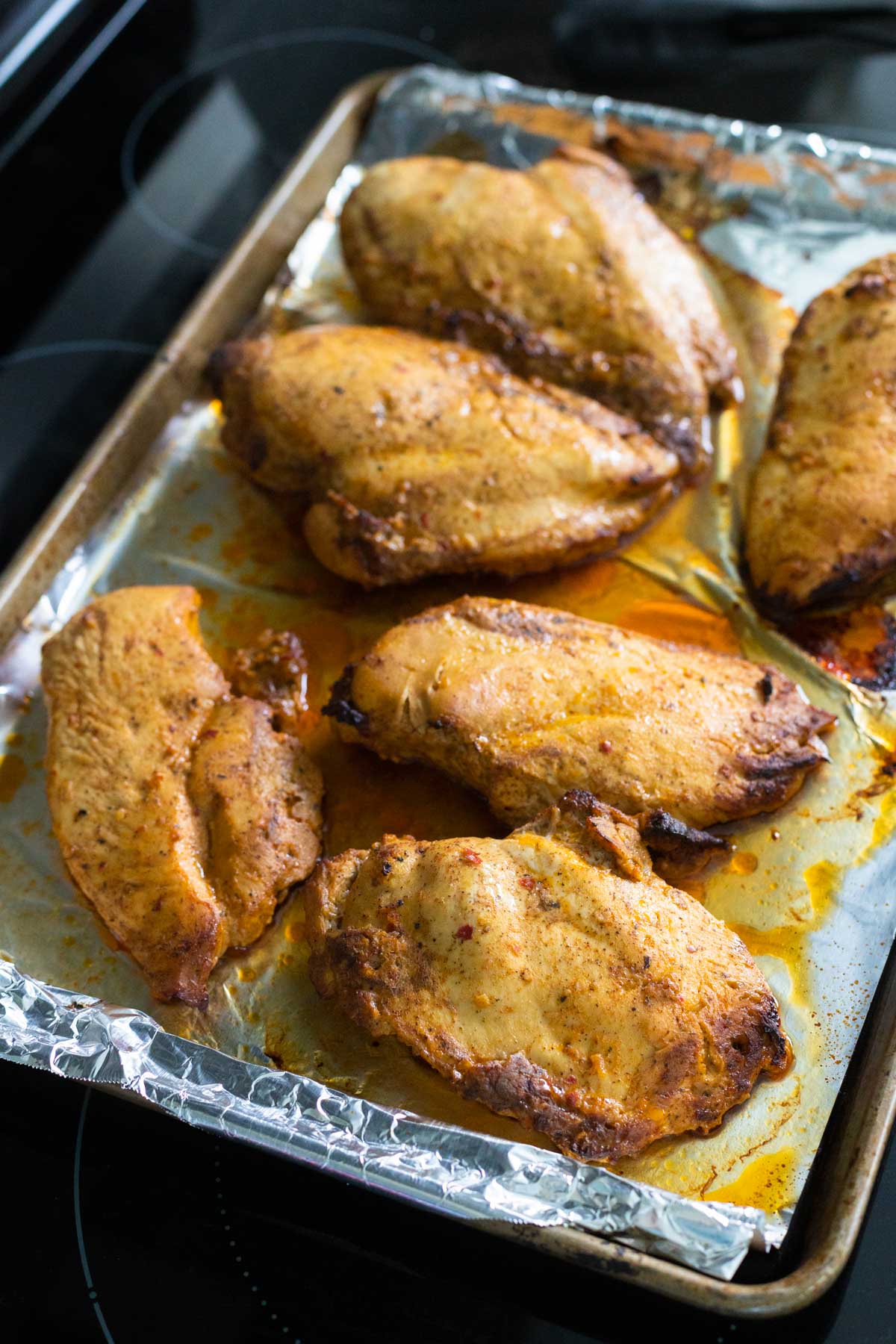 Seasoned chicken is on a large roasting pan lined with foil.