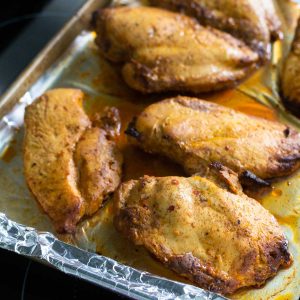A baking pan lined with foil has finished baked chicken breasts on top.