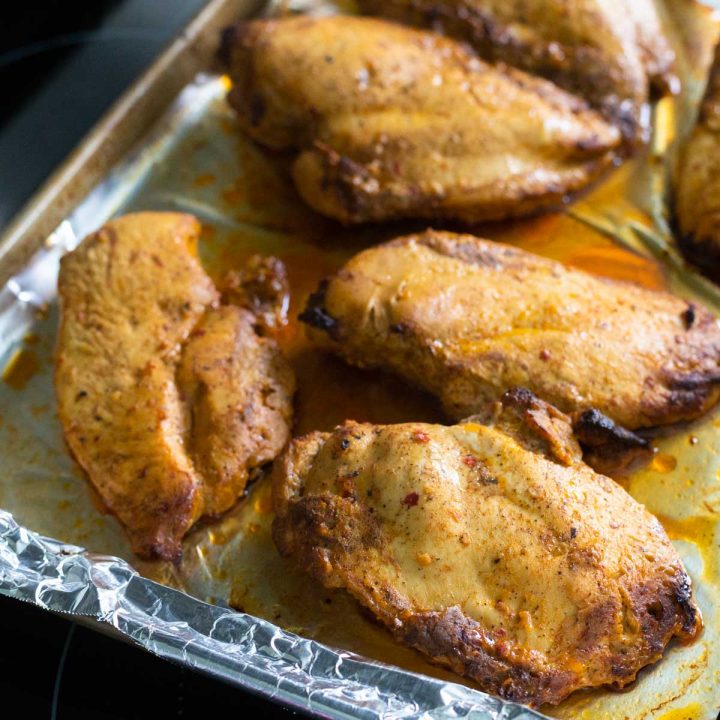A baking pan lined with foil has finished baked chicken breasts on top.