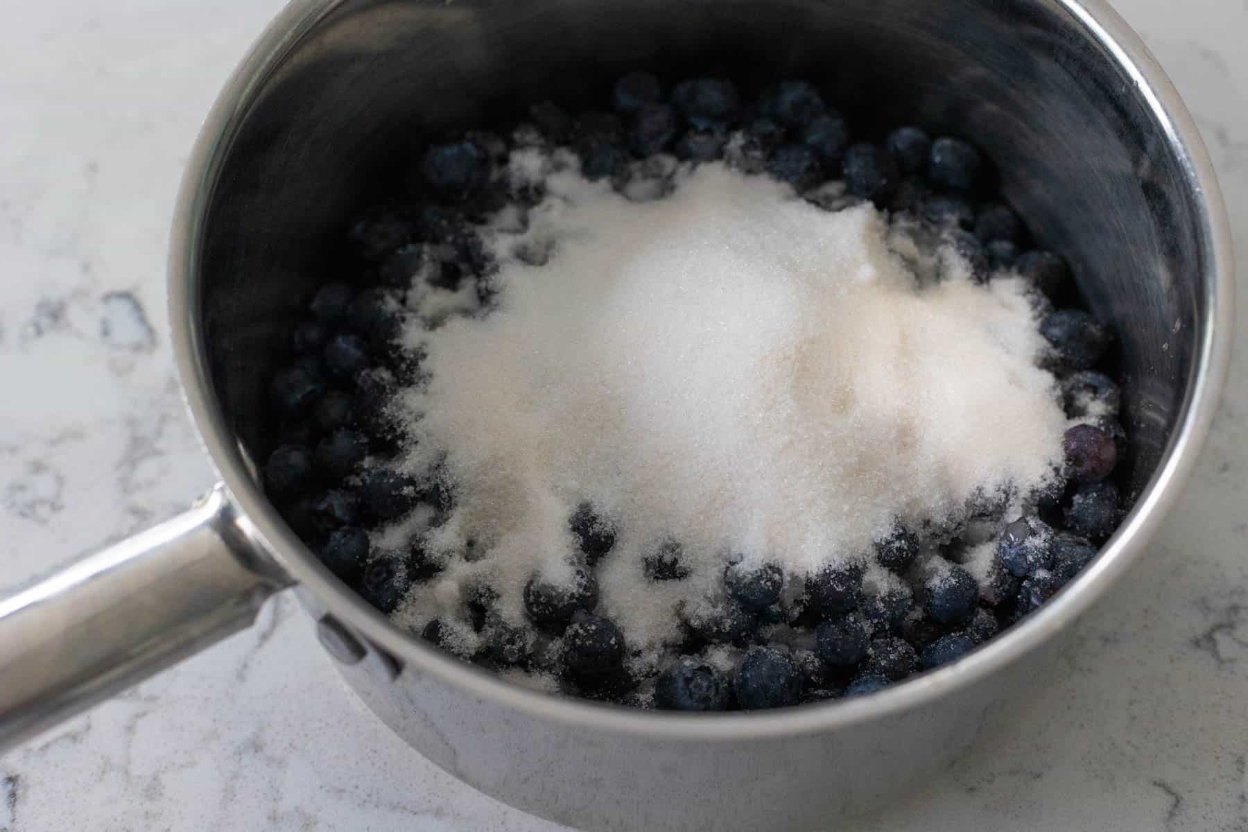 The sugar mixture has been poured over the blueberries in a saucepan.
