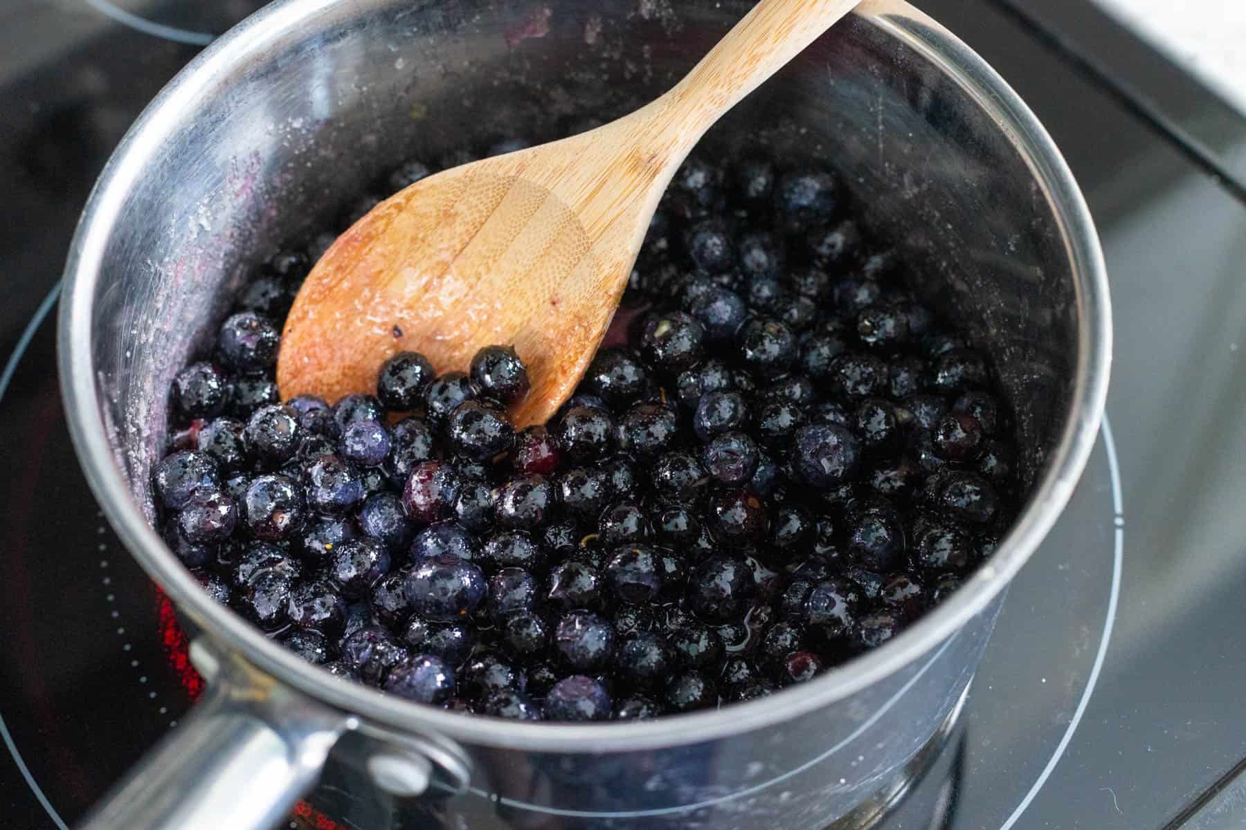 The blueberries are being stirred by a wooden spoon.