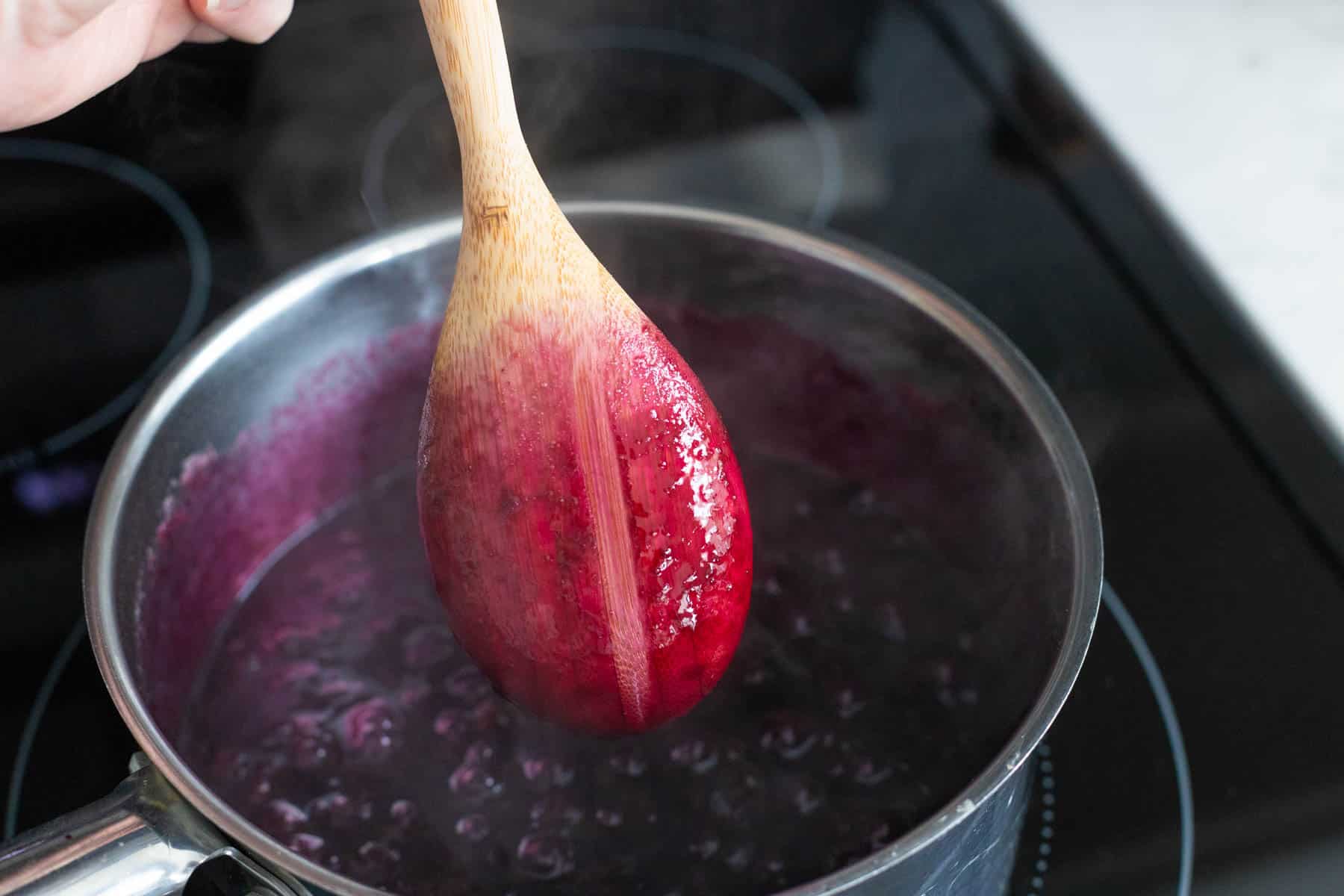 The cooking spoon has a clean swipe down the center that shows the blueberry preserves are thickened and ready.