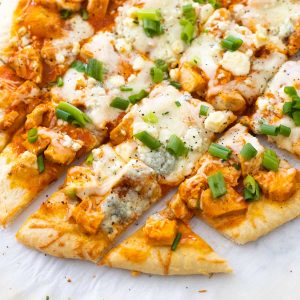 A sliced buffalo chicken flatbread has chunks of chicken, green onions, and melted cheese.