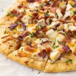 A baked chicken ranch pizza has chopped bacon and chicken chunks on top.
