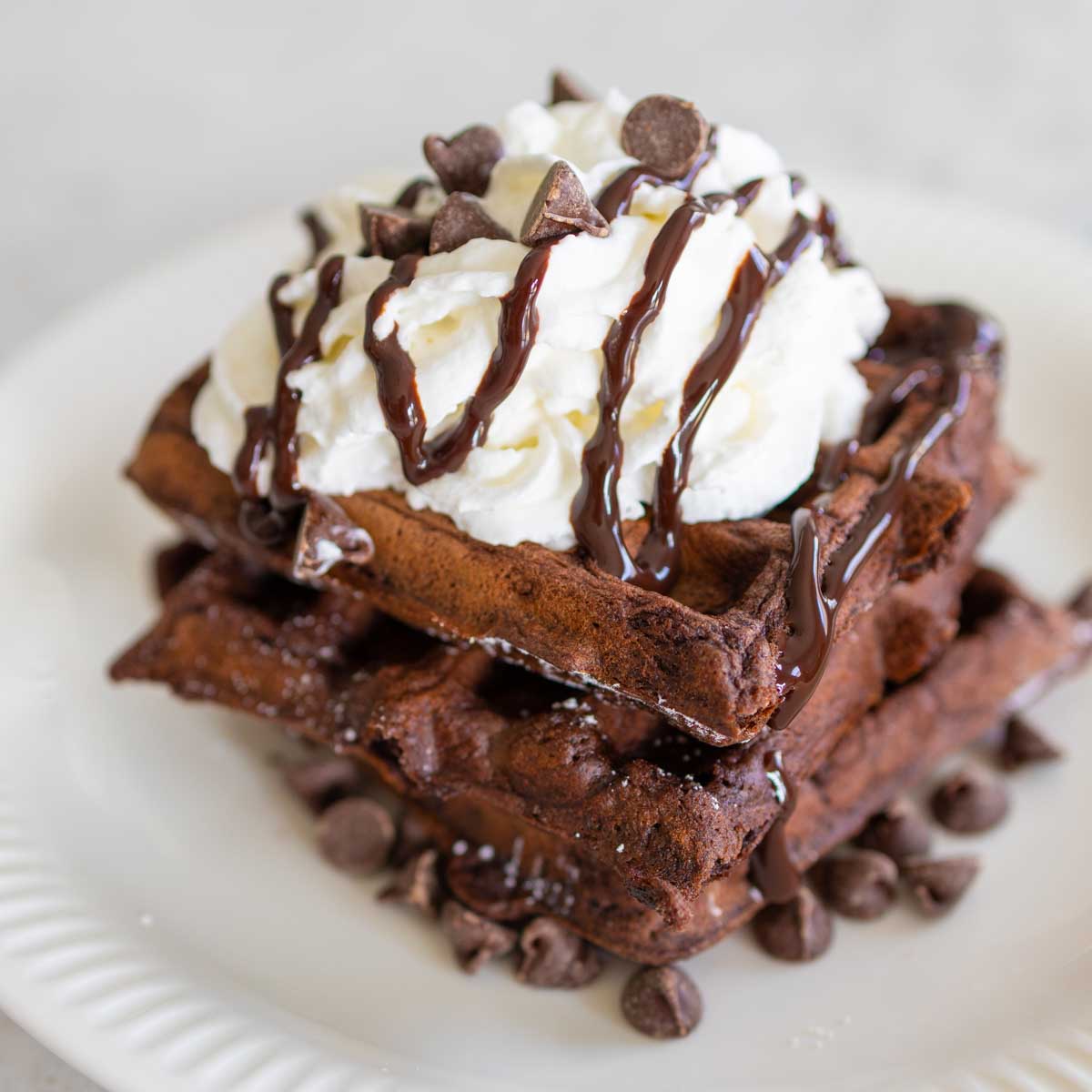 A stack of Belgian Chocolate Waffles with whipped cream and a chocolate drizzle.
