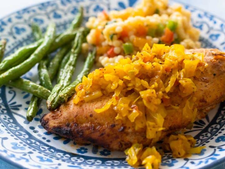 The chow chow has been spooned over a baked chicken breast. Green beans and a couscous side dish are in the background.