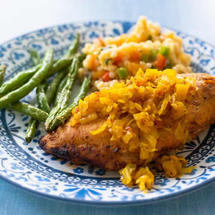 The chow chow has been spooned over a baked chicken breast. Green beans and a couscous side dish are in the background.