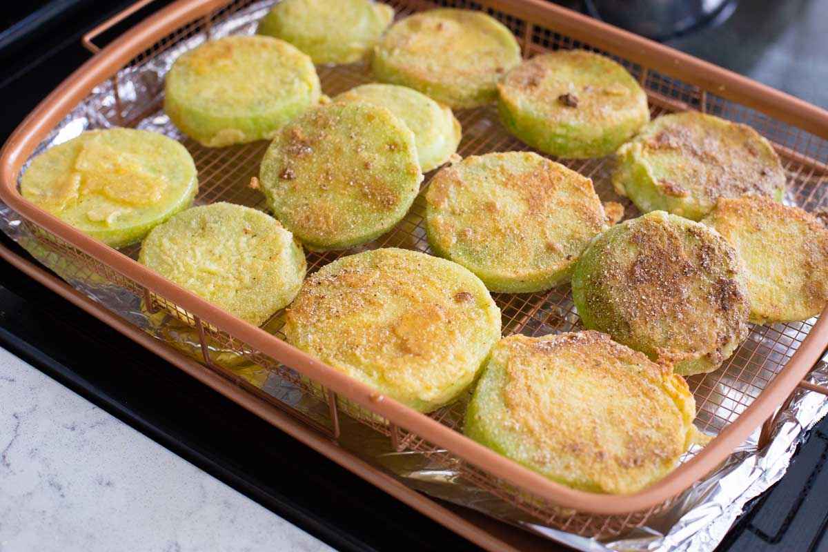 The green tomato slices are in an air fryer basket ready for the air fryer oven.