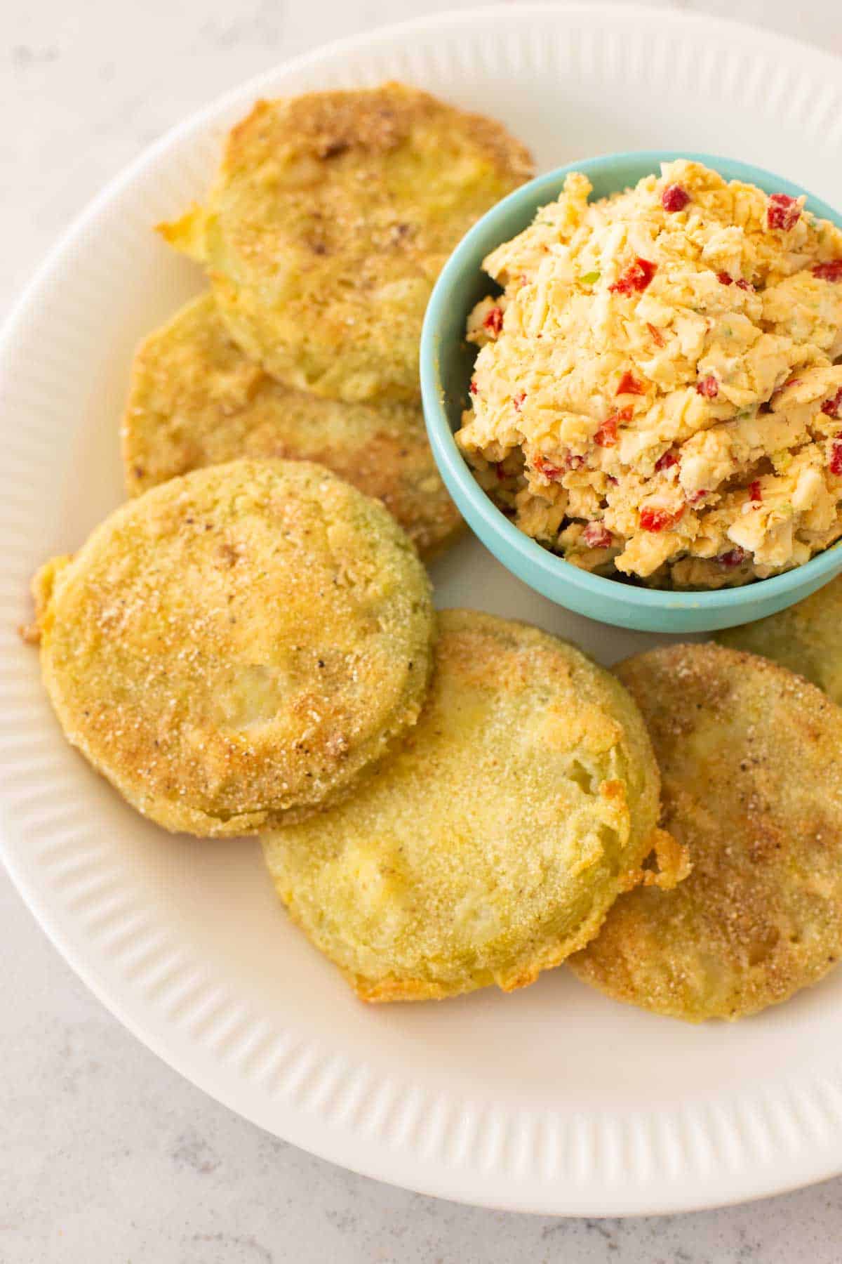 The southern fried green tomatoes are on a white plate with a bowl of pimiento cheese.