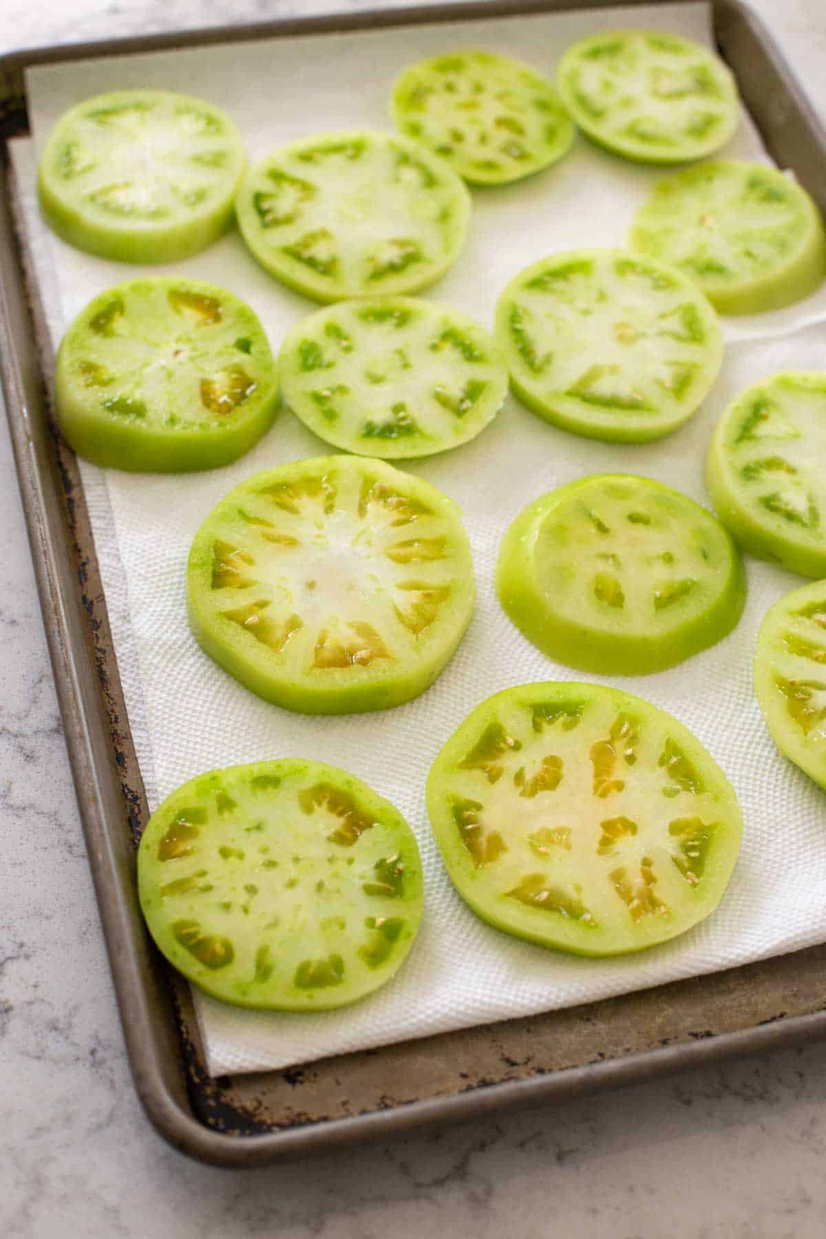 The tomato slices are draining on paper towels on a baking pan.