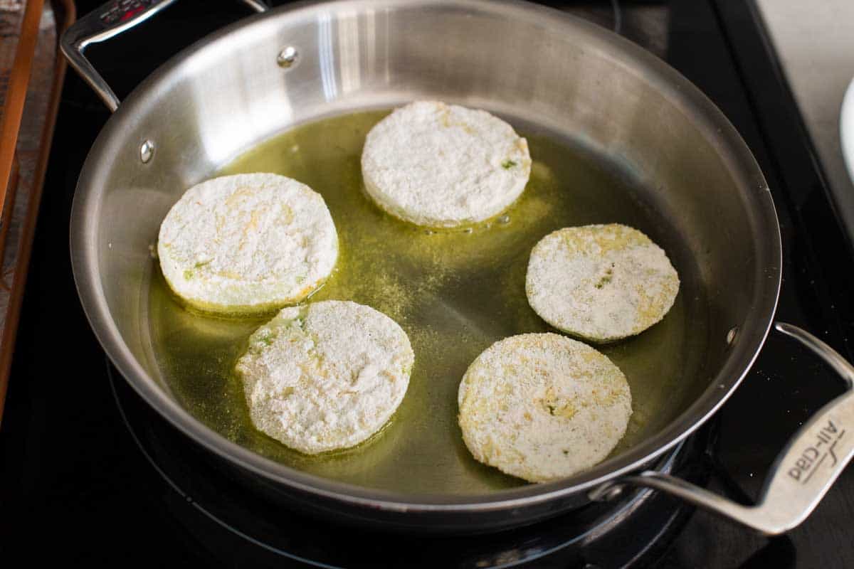 The large skillet filled with oil has 5 tomatoes frying.